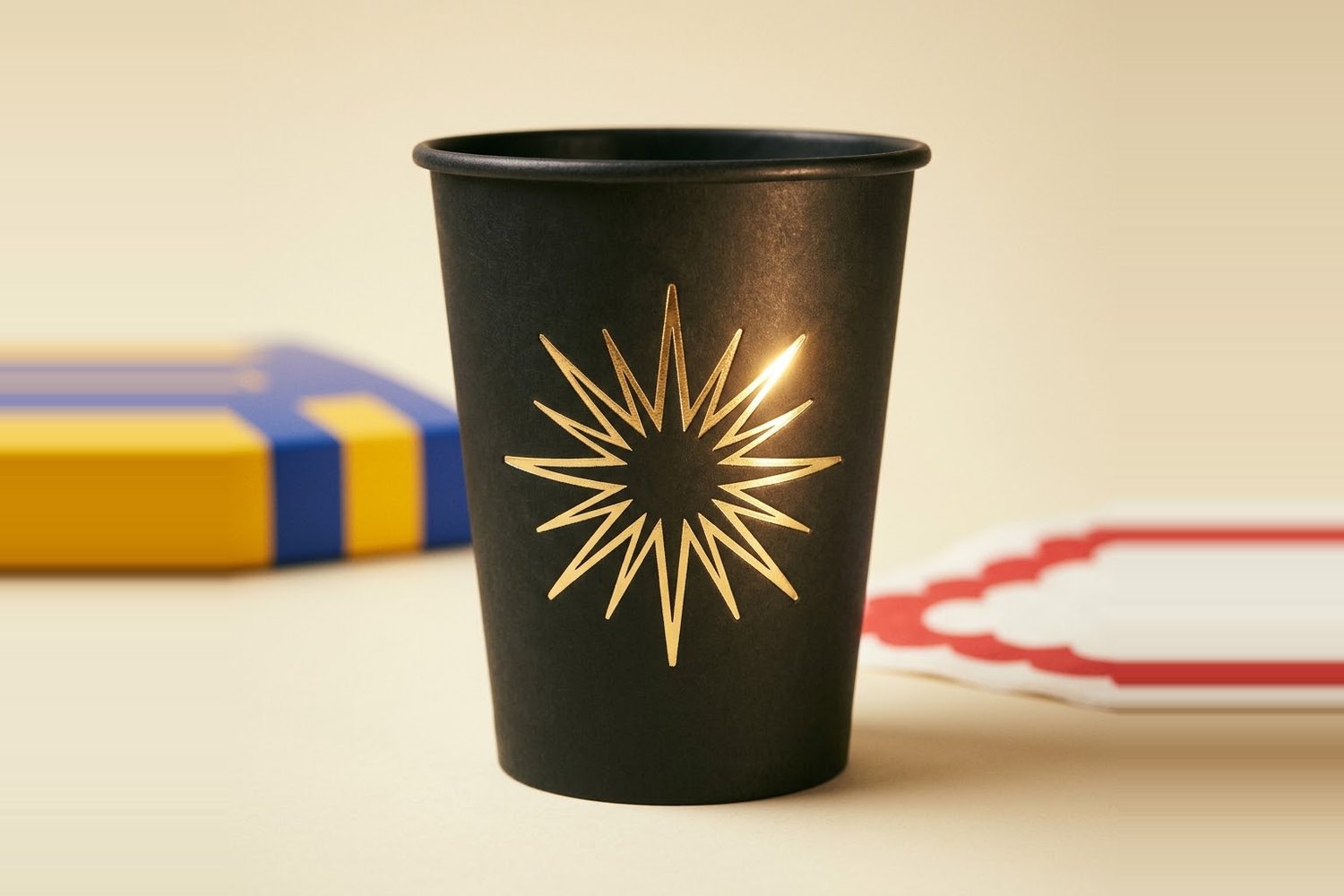Matte black paper cup with a gold hot-foil starburst, catching the light